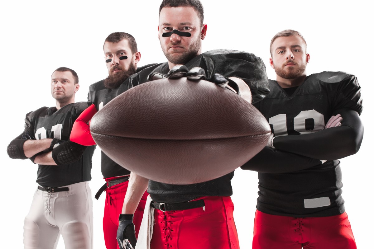four-caucasian-fitness-men-as-american-football-players-posing-full-length-with-ball-white (1)